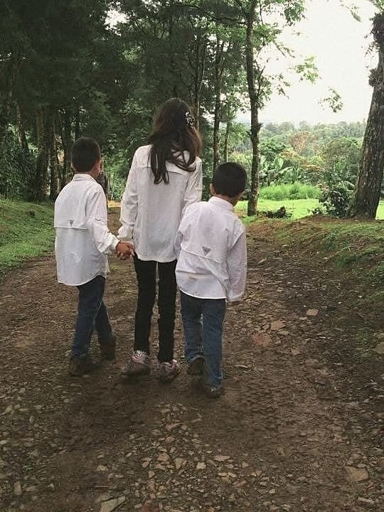 Three children in white shirts walking away from the camera up a dirt path between trees